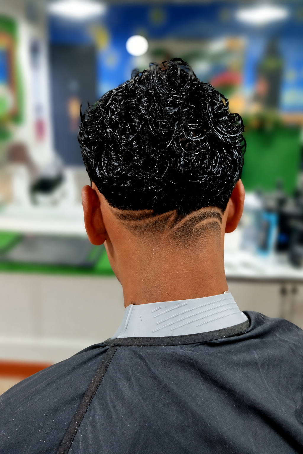 Corte de cabello rizado con diseño de líneas en la nuca realizado en Rocky&Chely